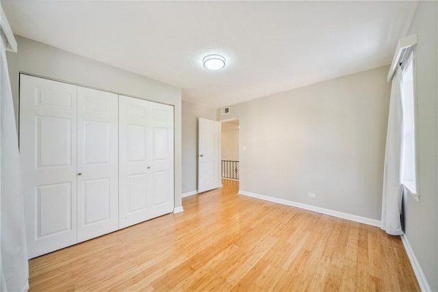 unfurnished bedroom featuring light wood-type flooring, baseboards, visible vents, and a closet