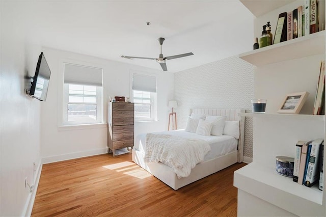 bedroom featuring light wood-style floors, an accent wall, ceiling fan, and baseboards