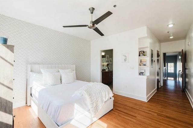bedroom featuring wallpapered walls, an accent wall, baseboards, and wood finished floors