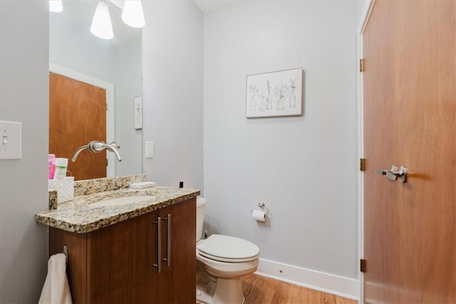 half bath with toilet, wood finished floors, vanity, and baseboards