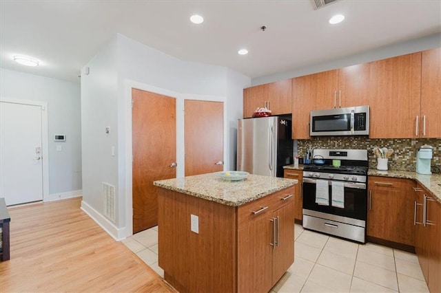 kitchen featuring light stone counters, a center island, brown cabinets, decorative backsplash, and stainless steel appliances