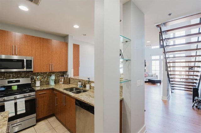 kitchen featuring light stone countertops, tasteful backsplash, a sink, stainless steel appliances, and brown cabinets