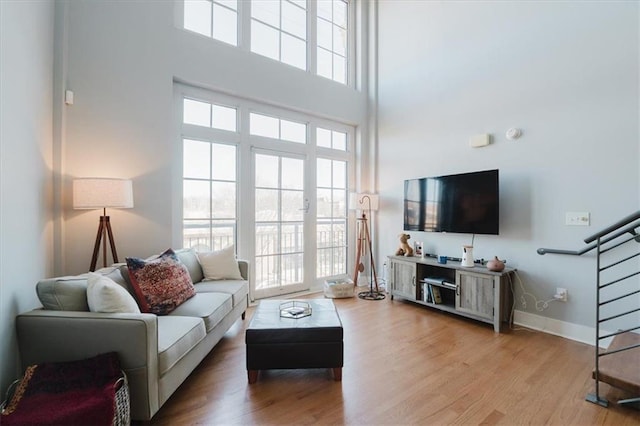 living area featuring stairway, a towering ceiling, baseboards, and wood finished floors