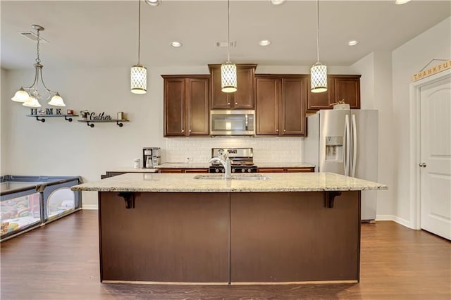 kitchen with a sink, dark wood-style flooring, light stone countertops, backsplash, and stainless steel appliances