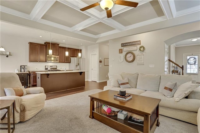 living room with arched walkways, ornamental molding, ceiling fan, beam ceiling, and coffered ceiling