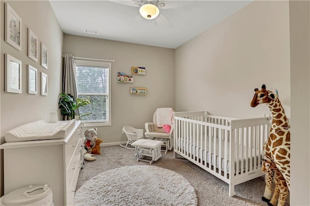carpeted bedroom featuring visible vents, baseboards, a ceiling fan, and a crib