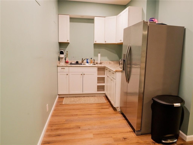 kitchen with stainless steel fridge, light countertops, white cabinets, light wood finished floors, and a sink