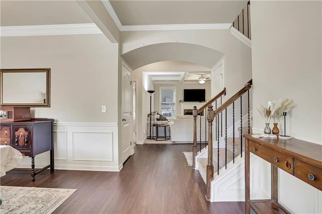 entrance foyer featuring ceiling fan, arched walkways, ornamental molding, stairway, and dark wood-style floors