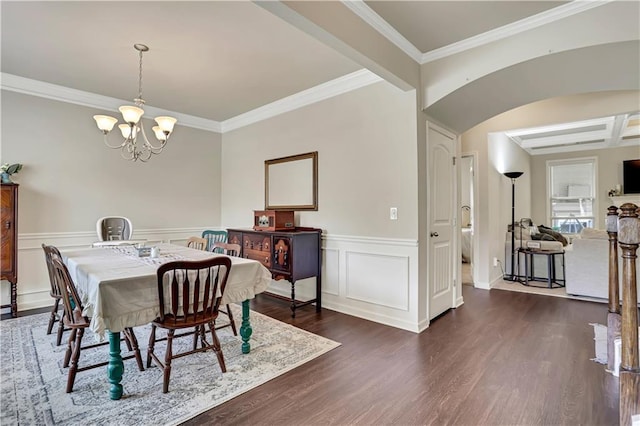 dining space with crown molding, a notable chandelier, dark wood finished floors, and a wainscoted wall