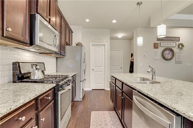 kitchen with appliances with stainless steel finishes, light stone counters, a sink, decorative backsplash, and dark wood-style floors