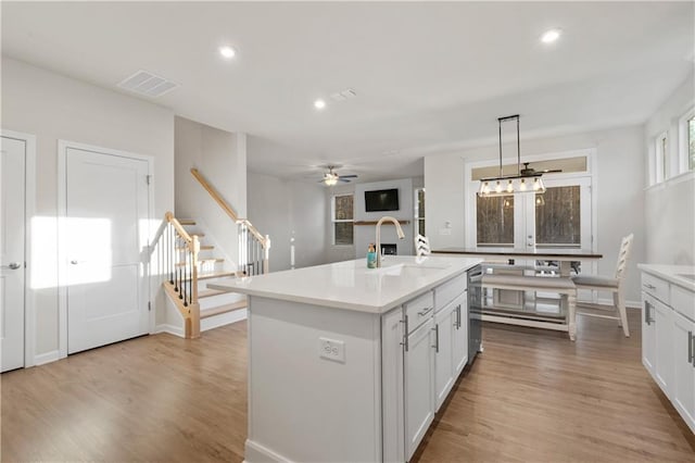 kitchen with sink, white cabinetry, light wood-type flooring, pendant lighting, and a kitchen island with sink