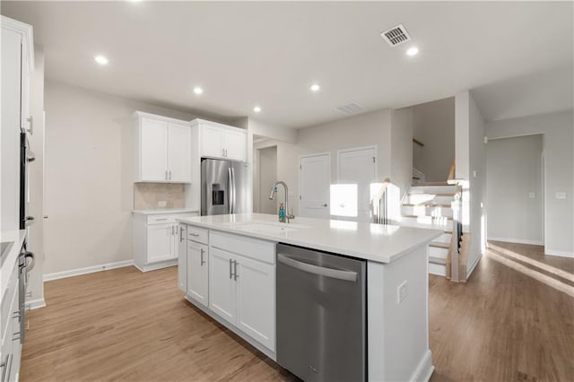 kitchen with appliances with stainless steel finishes, an island with sink, sink, white cabinets, and light wood-type flooring