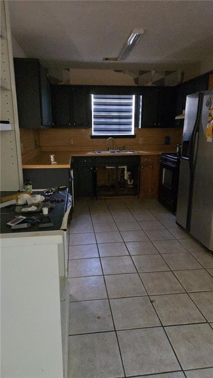 kitchen featuring freestanding refrigerator, light tile patterned flooring, black range oven, light countertops, and a sink