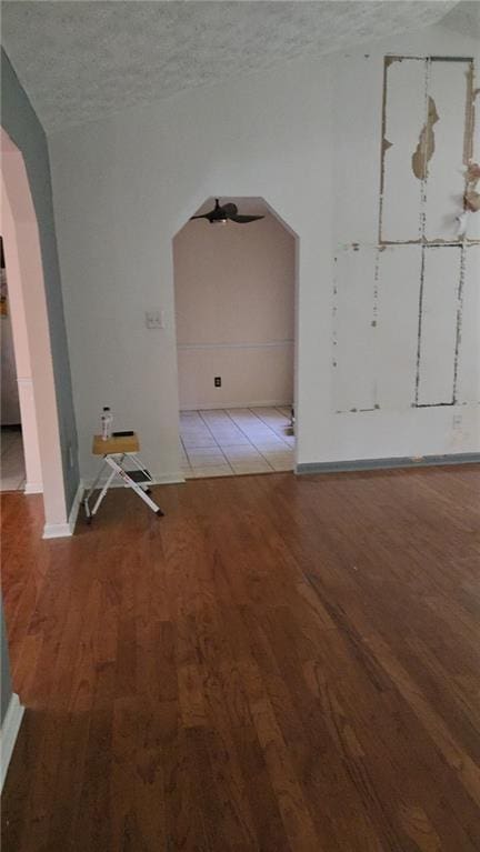 spare room with baseboards, arched walkways, a textured ceiling, and wood finished floors