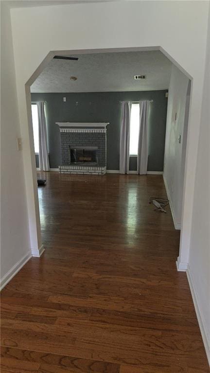 unfurnished living room with a brick fireplace, visible vents, and wood finished floors