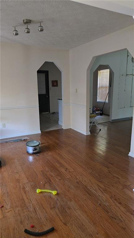 interior space featuring arched walkways, baseboards, wood finished floors, and a textured ceiling