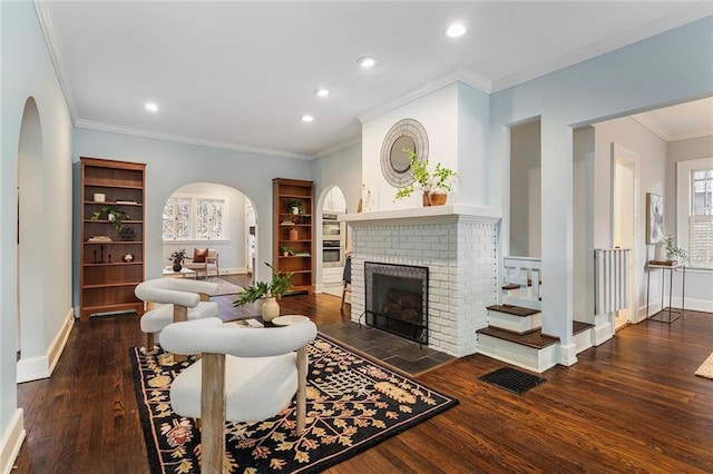 living room with ornamental molding, dark hardwood / wood-style flooring, a brick fireplace, and built in shelves