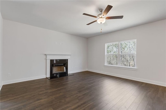 unfurnished living room with baseboards, a fireplace, a ceiling fan, and dark wood-style floors