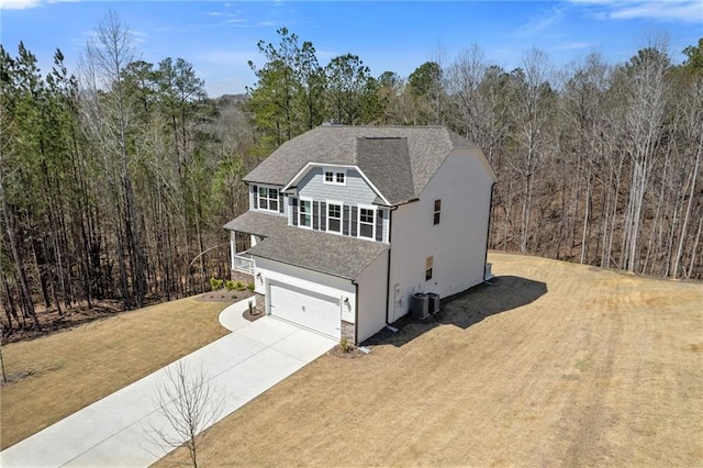 view of front of home featuring a shingled roof, a front lawn, a garage, concrete driveway, and a forest view