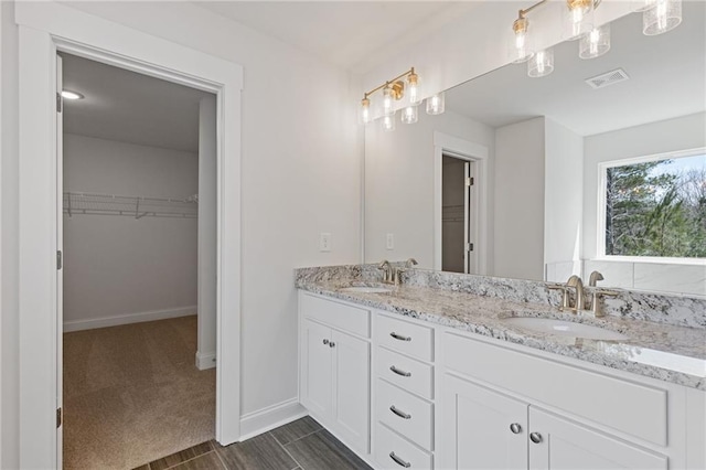bathroom with a sink, a walk in closet, double vanity, and visible vents