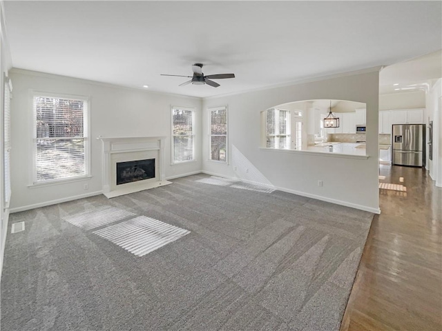 unfurnished living room featuring a fireplace with raised hearth, a healthy amount of sunlight, baseboards, and crown molding