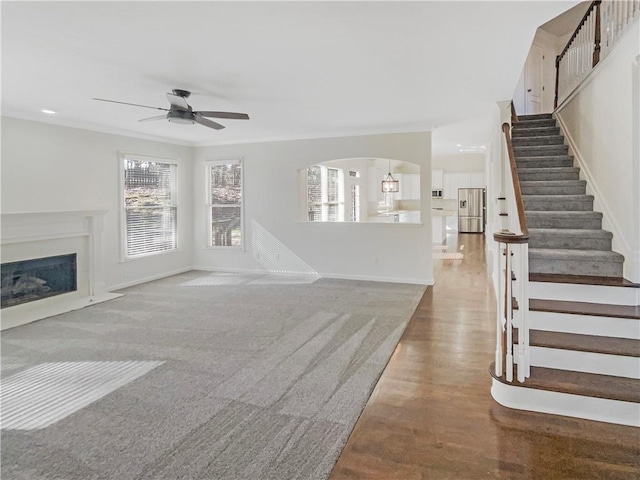 unfurnished living room with baseboards, a fireplace with flush hearth, stairway, and a ceiling fan