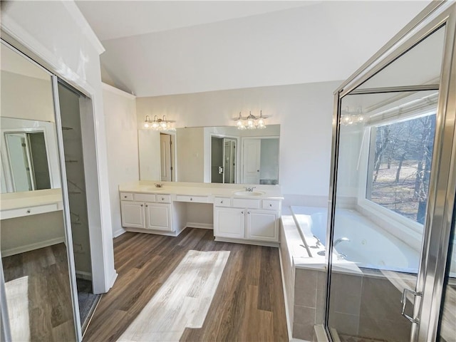 bathroom featuring double vanity, lofted ceiling, a tub with jets, wood finished floors, and a sink