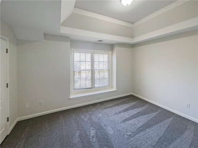 empty room featuring visible vents, dark carpet, a raised ceiling, and baseboards