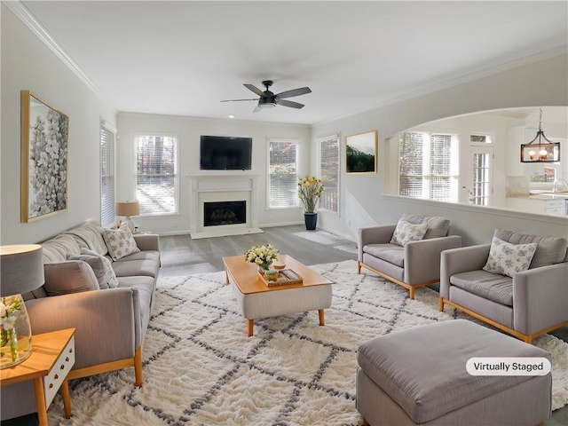 living room featuring ornamental molding, a fireplace, and ceiling fan with notable chandelier