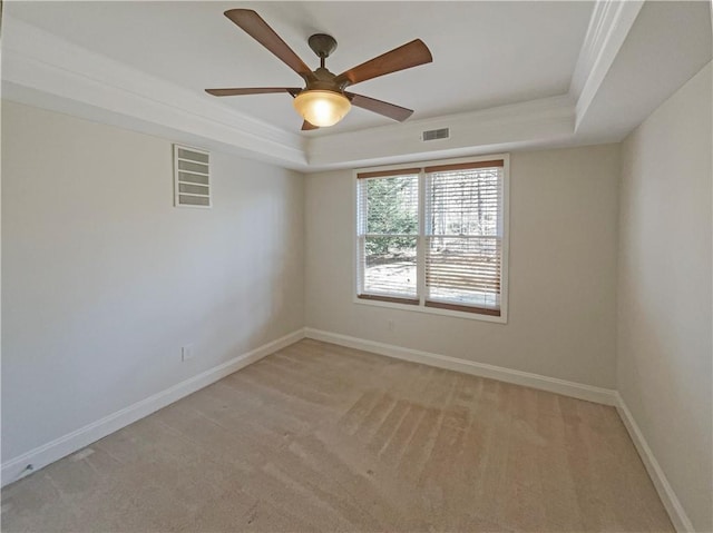 unfurnished room with visible vents, a tray ceiling, baseboards, and light colored carpet