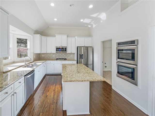 kitchen with stainless steel appliances, a kitchen island, white cabinetry, and light stone countertops