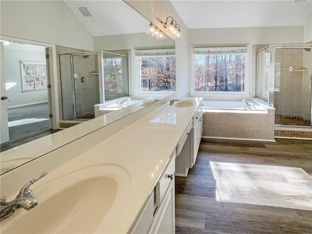 bathroom with double vanity, wood finished floors, a garden tub, vaulted ceiling, and a sink