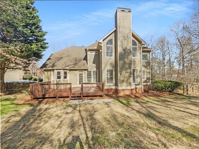 back of house featuring a lawn, a chimney, fence, and a wooden deck