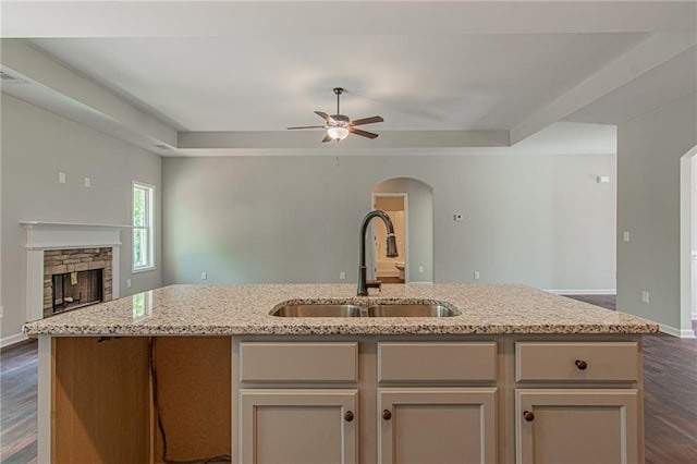 kitchen with a center island with sink, a sink, light stone counters, open floor plan, and arched walkways