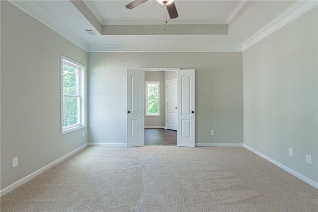 carpeted empty room featuring baseboards, visible vents, ceiling fan, ornamental molding, and a raised ceiling