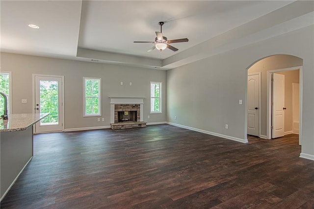 unfurnished living room with a raised ceiling, baseboards, dark wood-type flooring, and ceiling fan