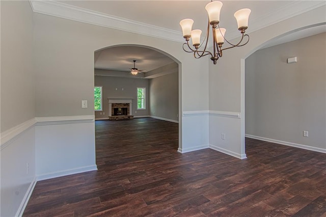 unfurnished room featuring a fireplace with raised hearth, baseboards, ceiling fan with notable chandelier, wood finished floors, and arched walkways