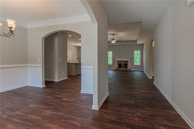 hall with baseboards, arched walkways, dark wood finished floors, and crown molding