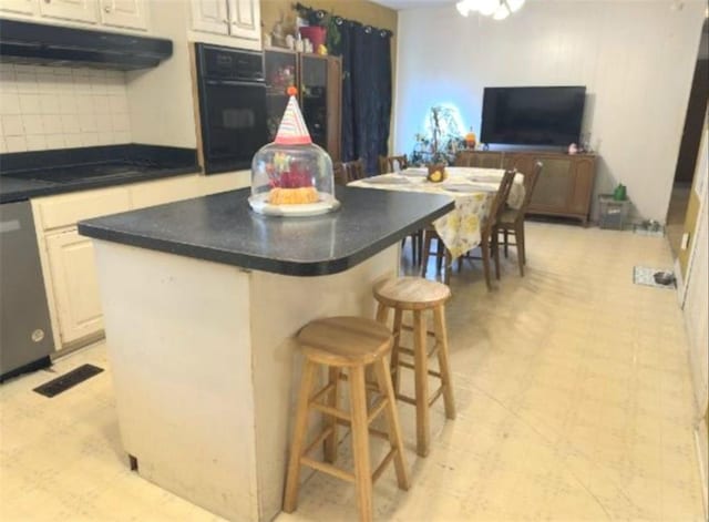 kitchen featuring under cabinet range hood, light floors, black appliances, and a breakfast bar