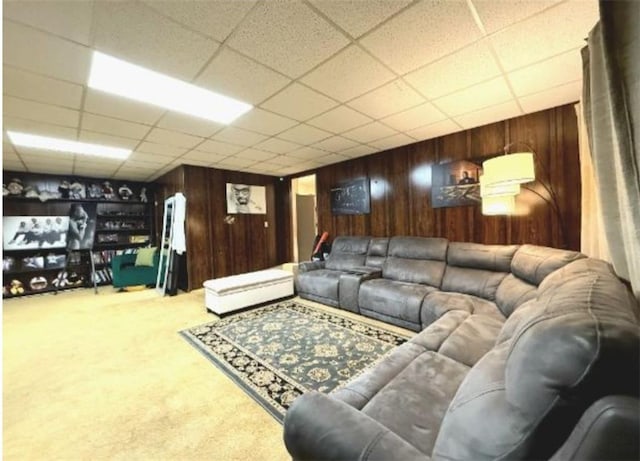 carpeted living room with a drop ceiling and wood walls