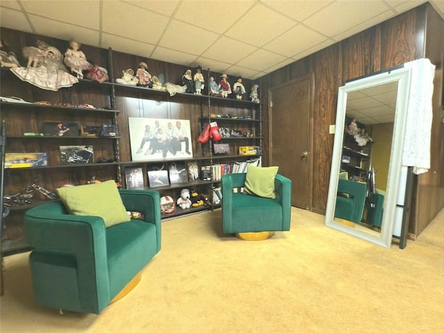 living area with carpet flooring, a paneled ceiling, and wooden walls