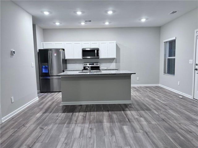 kitchen with stainless steel appliances, white cabinets, a center island with sink, and light stone counters