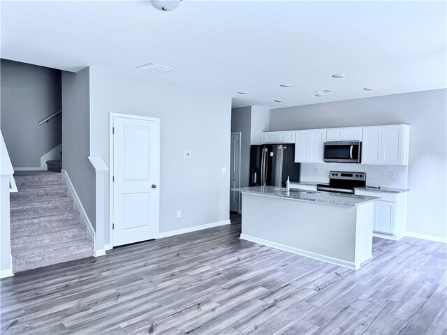 kitchen featuring light hardwood / wood-style flooring, a kitchen island with sink, white cabinetry, appliances with stainless steel finishes, and light stone countertops