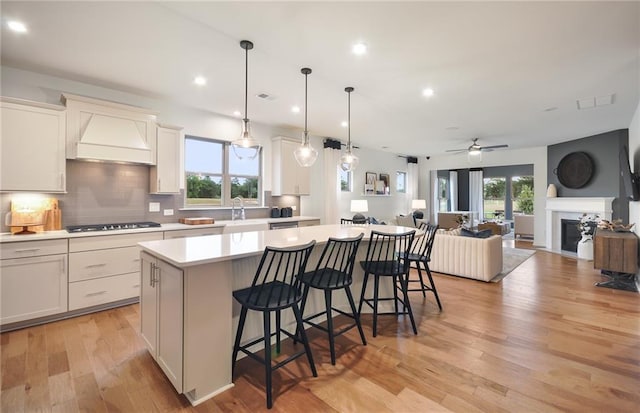 kitchen featuring a center island, a kitchen breakfast bar, custom range hood, ceiling fan, and black stovetop