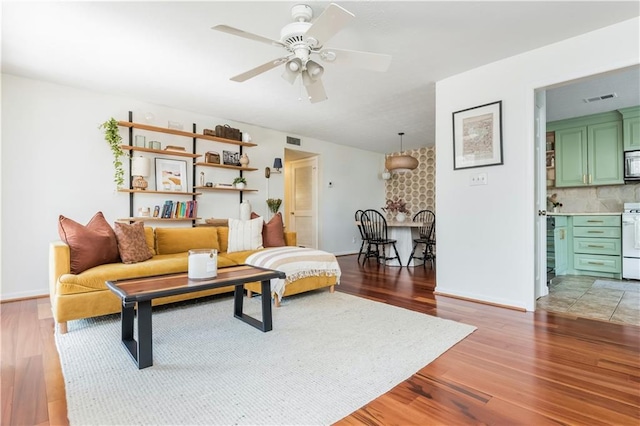 living room with a ceiling fan, visible vents, light wood-style flooring, and baseboards