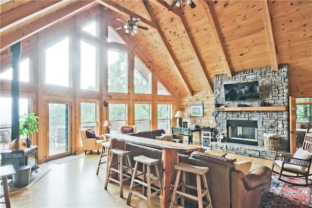 living room featuring wooden walls, hardwood / wood-style floors, beam ceiling, high vaulted ceiling, and a wood stove