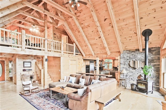 living room featuring a wood stove, beamed ceiling, high vaulted ceiling, wooden walls, and hardwood / wood-style flooring