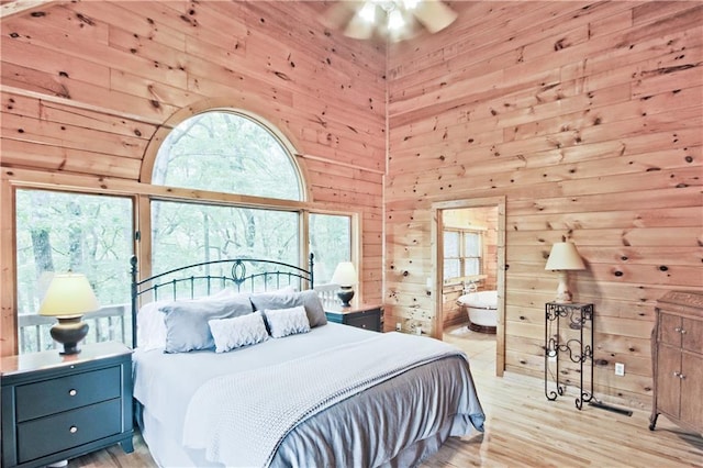 bedroom featuring connected bathroom, multiple windows, wood walls, and light hardwood / wood-style flooring