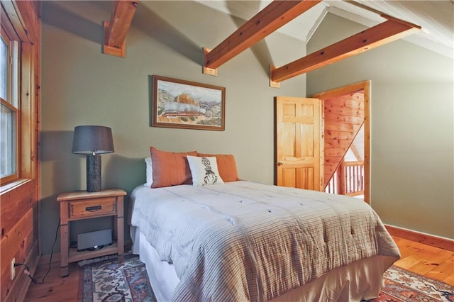 bedroom with hardwood / wood-style floors, vaulted ceiling with beams, wood walls, and multiple windows