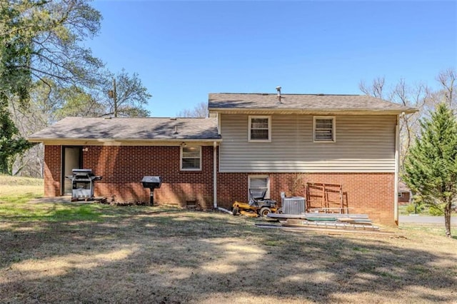 back of house with brick siding, central air condition unit, and a yard